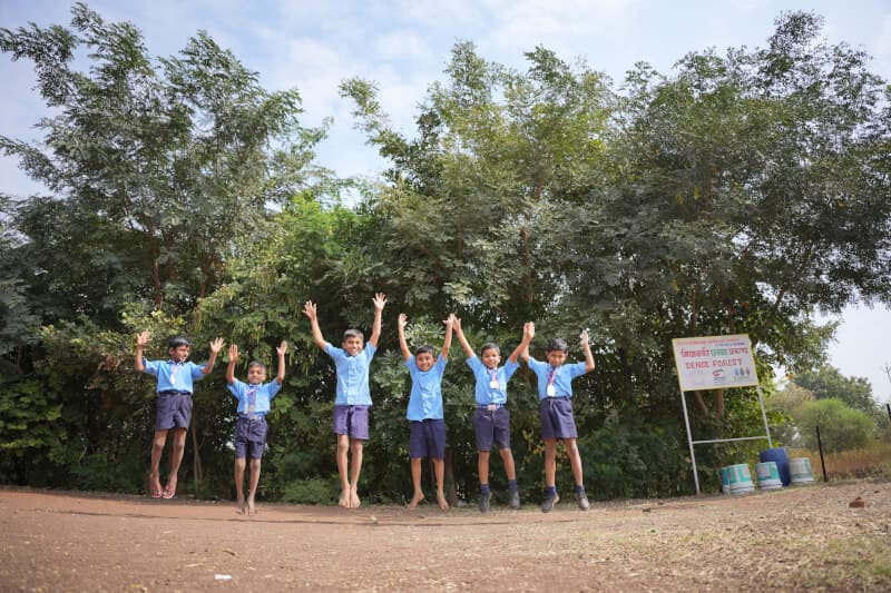 School kids jumping in the air in front of a Miyawaki Forest